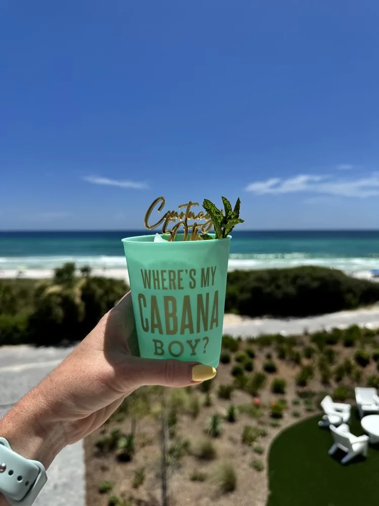 A cocktail in a 'Where's my cabana boy?' cup held up over the Gulf